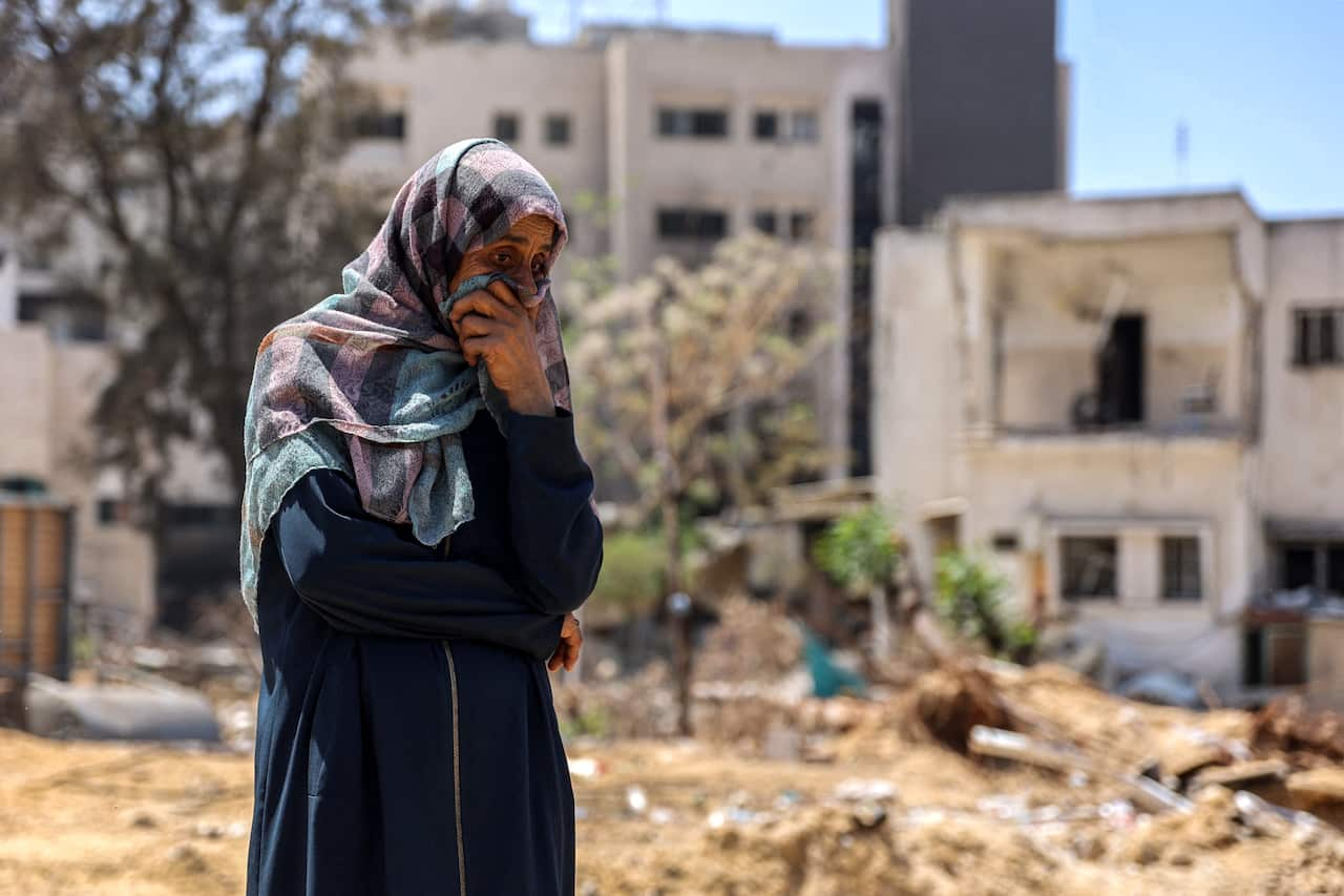 A person stands in rubble with a headscarf on