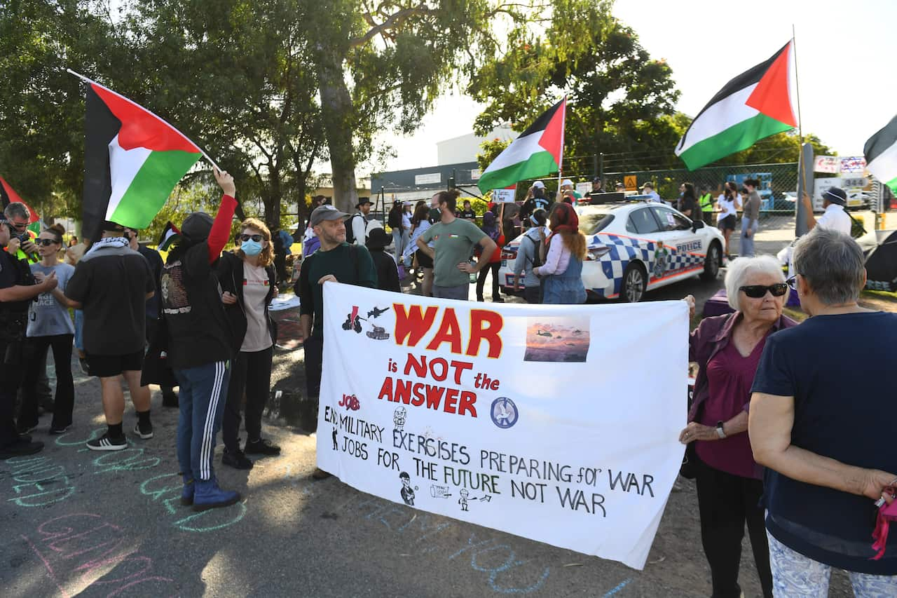 A group of people waving Palestinian flags with a large banner that reads "War is not the answer"