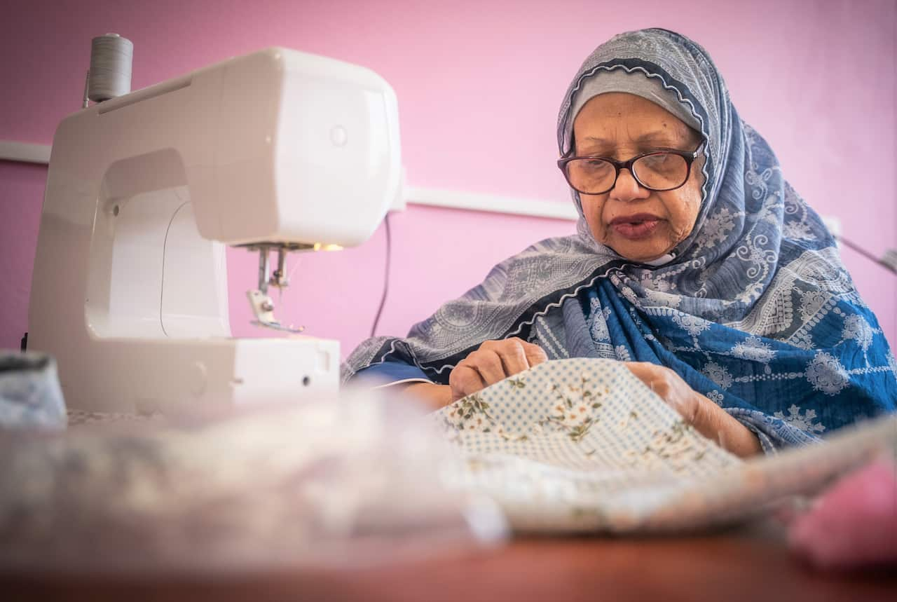 A woman sits at a sewing machine holding a piece of fabric. 