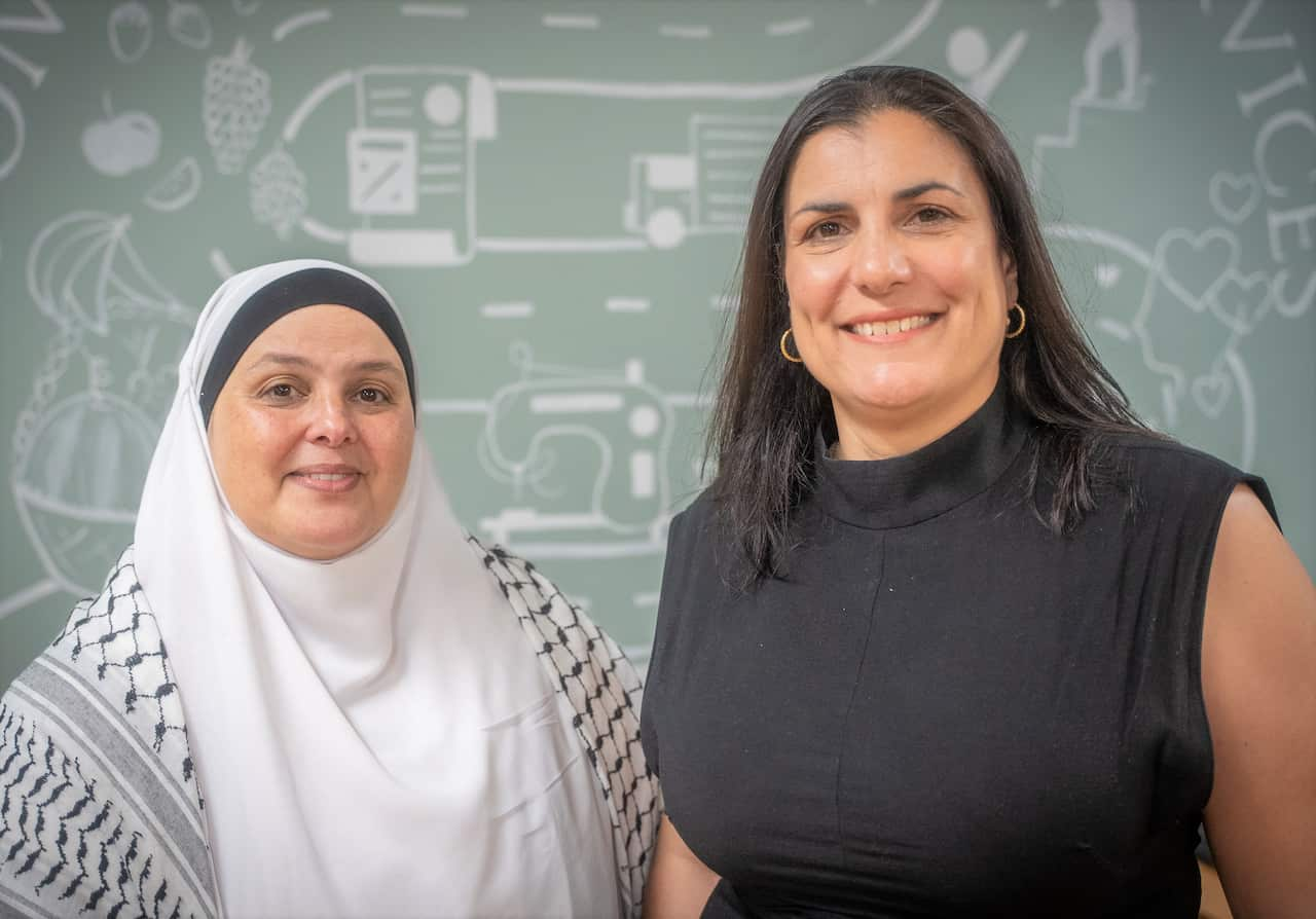 Two women stand in front of a mural in an office.