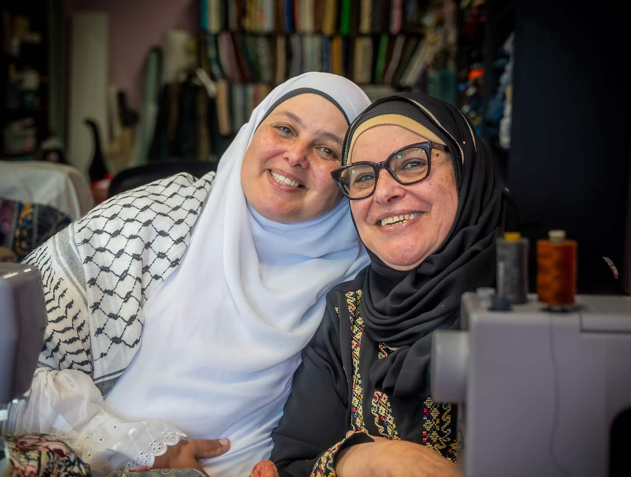 Two women sit at a sewing machine in a workshop.