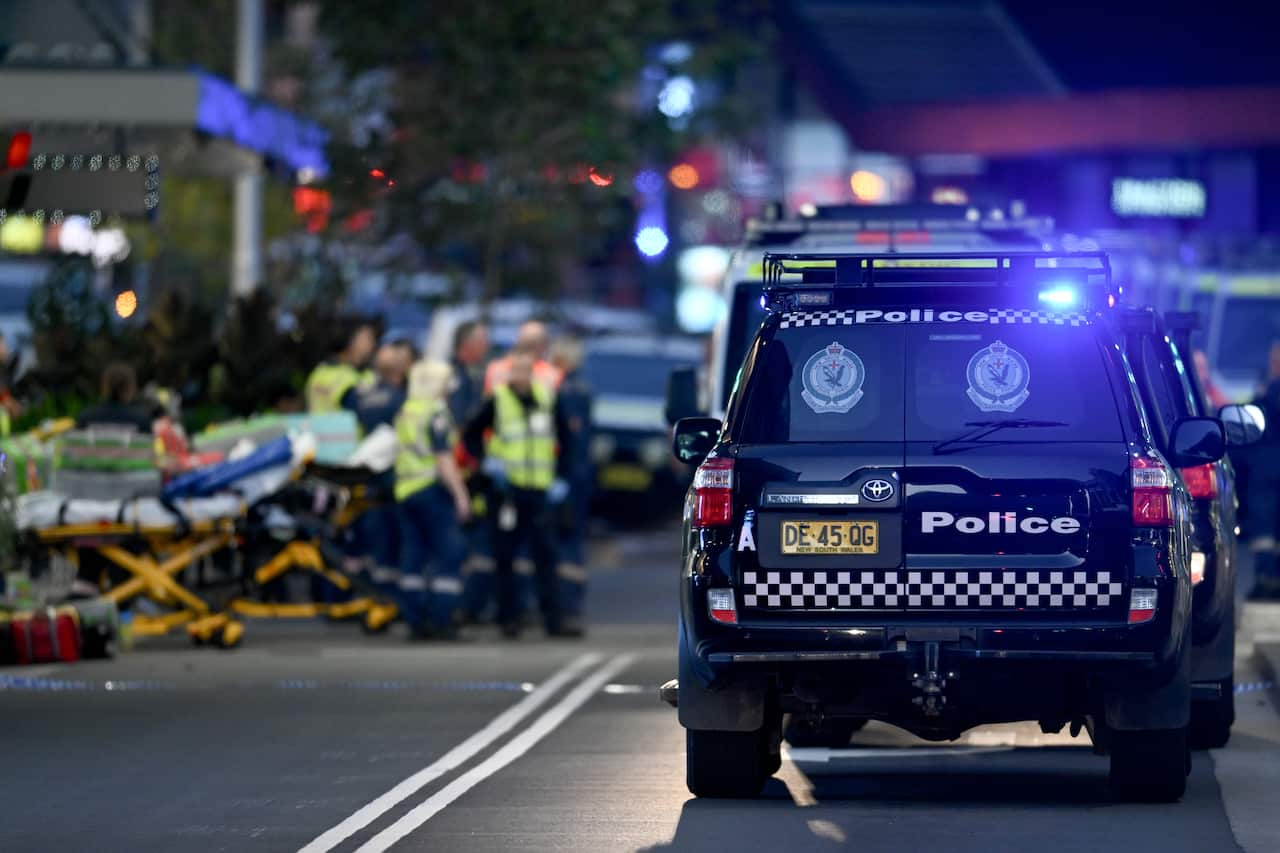 A group of first responders with stretchers on a street next to a police vehicle. 