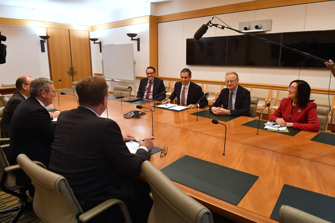 A group of politicians and finance leaders sit at a long wooden table.