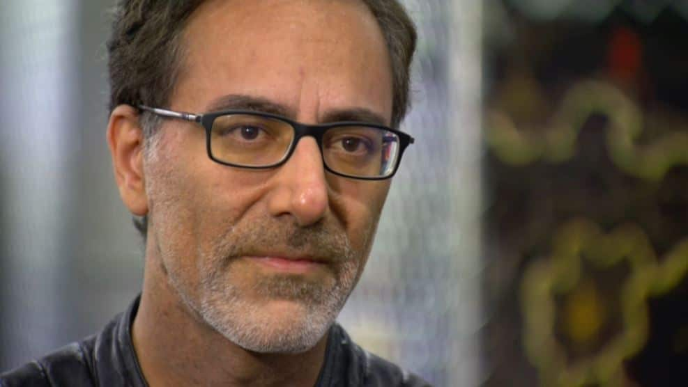 A man with black-rimmed glasses has a solemn expression.