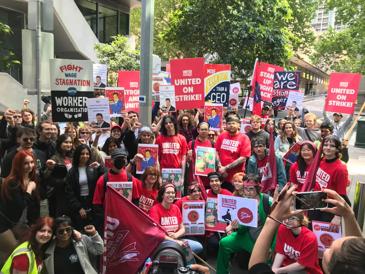 A large group of people, many of whom wear red T-shirts emblazoned with "United Workers Union" pose for a photograph.