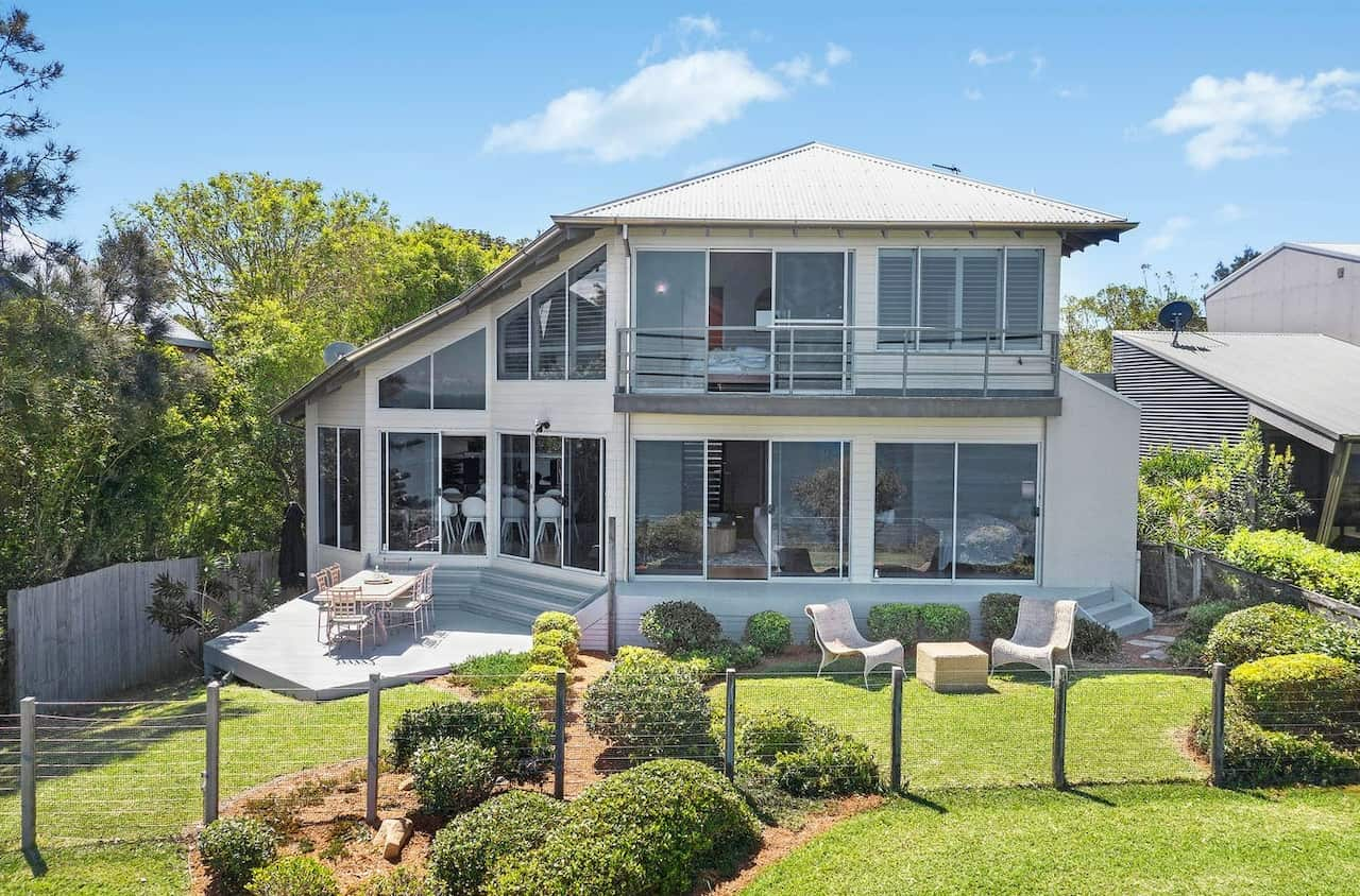 A double storey white weatherboard home, fenced off with a low clear fence.