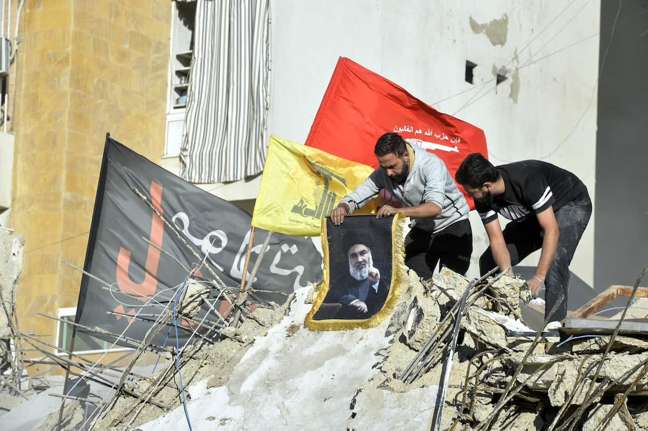 Two men are crouched amid the debris, one of them holding a poster.