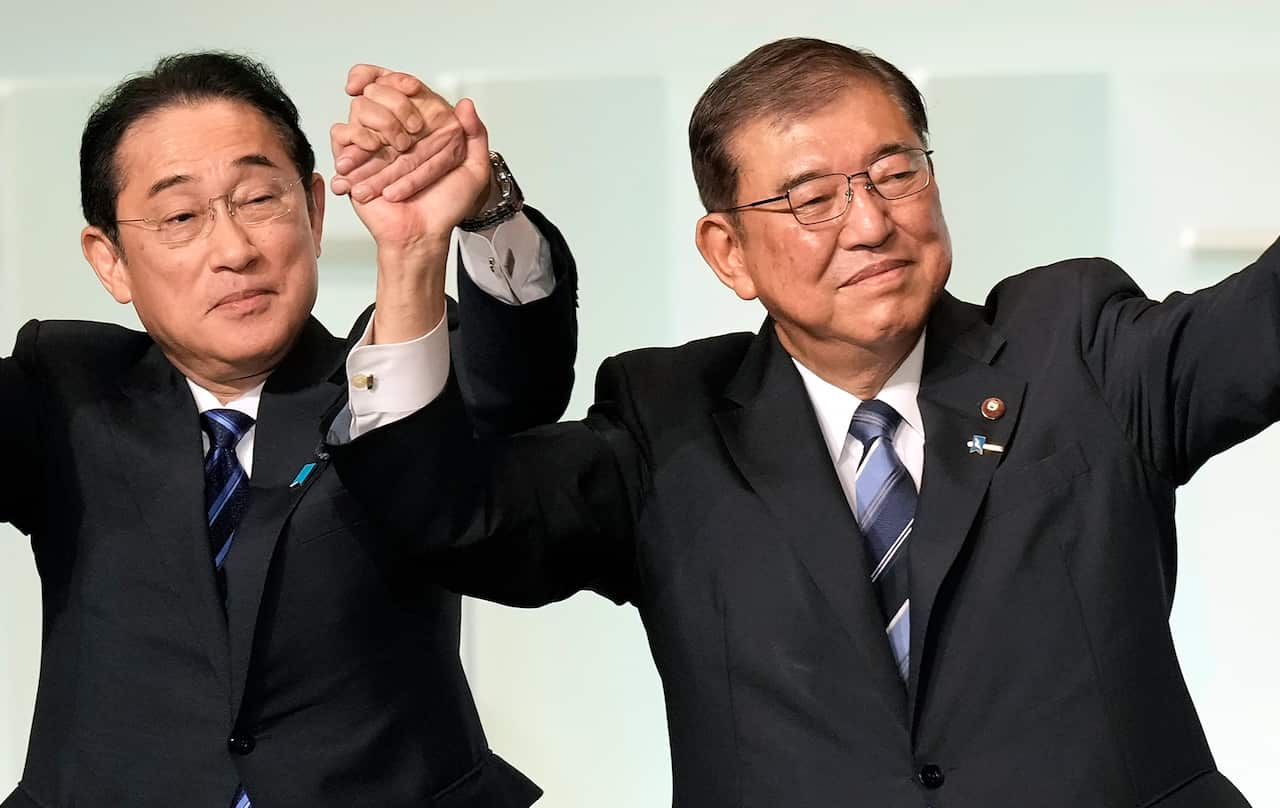 Two men in dark suits holding hands together in the air in celebration.