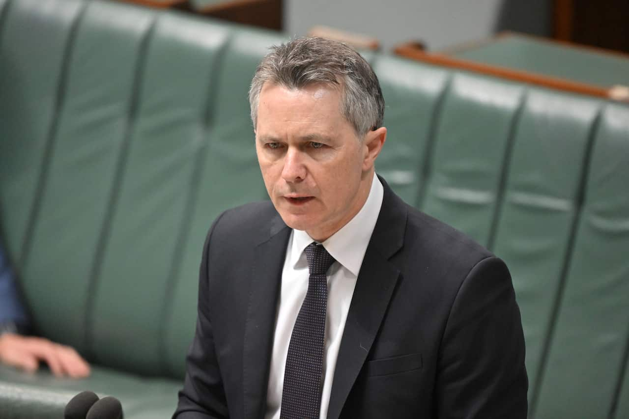 A man in a dark suit stands in front of green benches