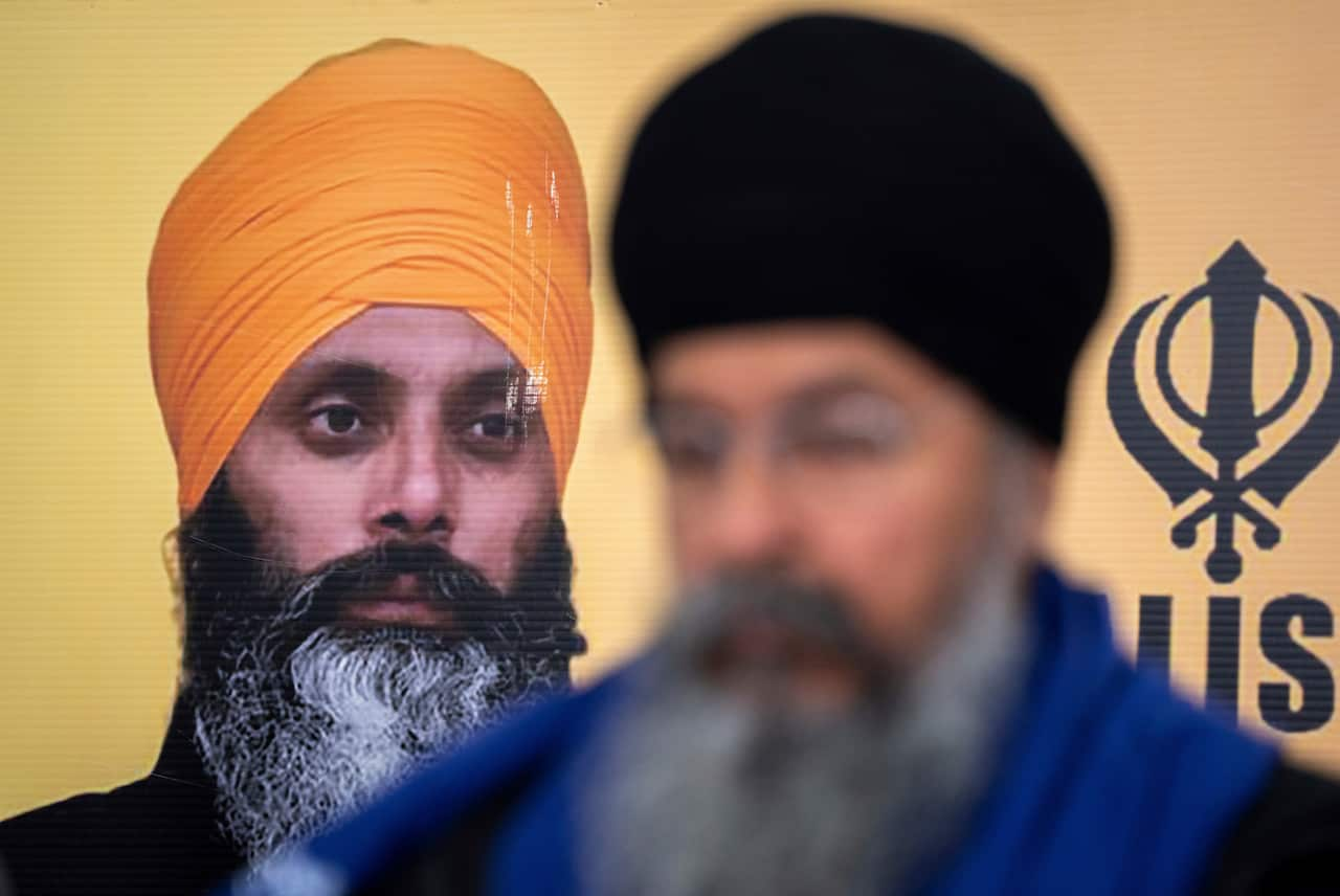 A Sikh man standing in front of a photo of another Sikh man.