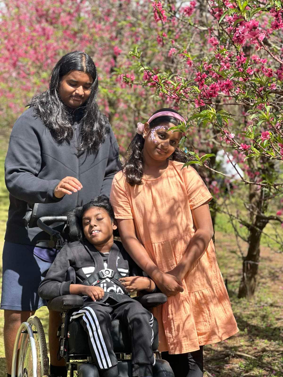 A male child in a wheelchair with his brother and sister standing next to him