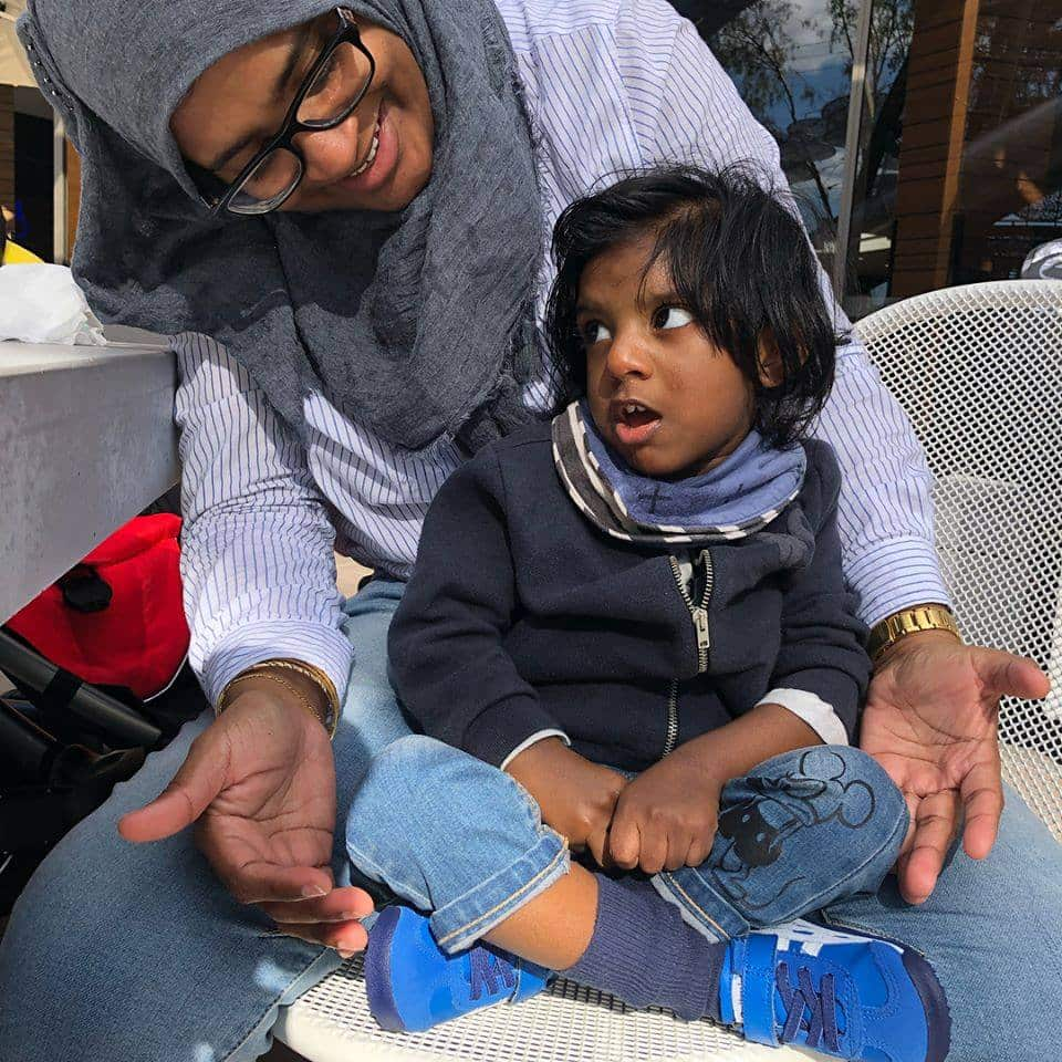 A young boy sits in his mother's lap on a chair.