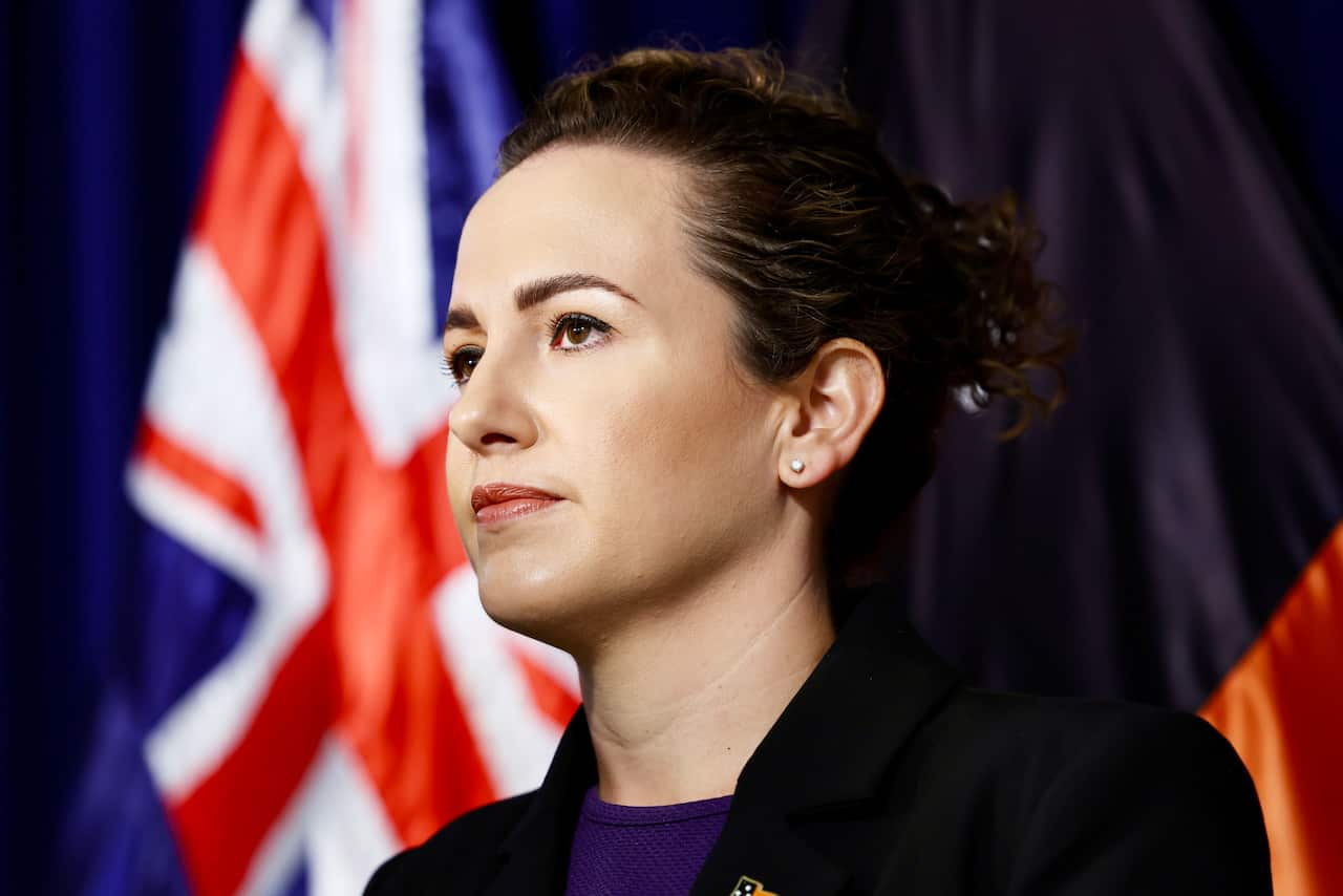 A woman staring ahead. An Australian flag is behind her.