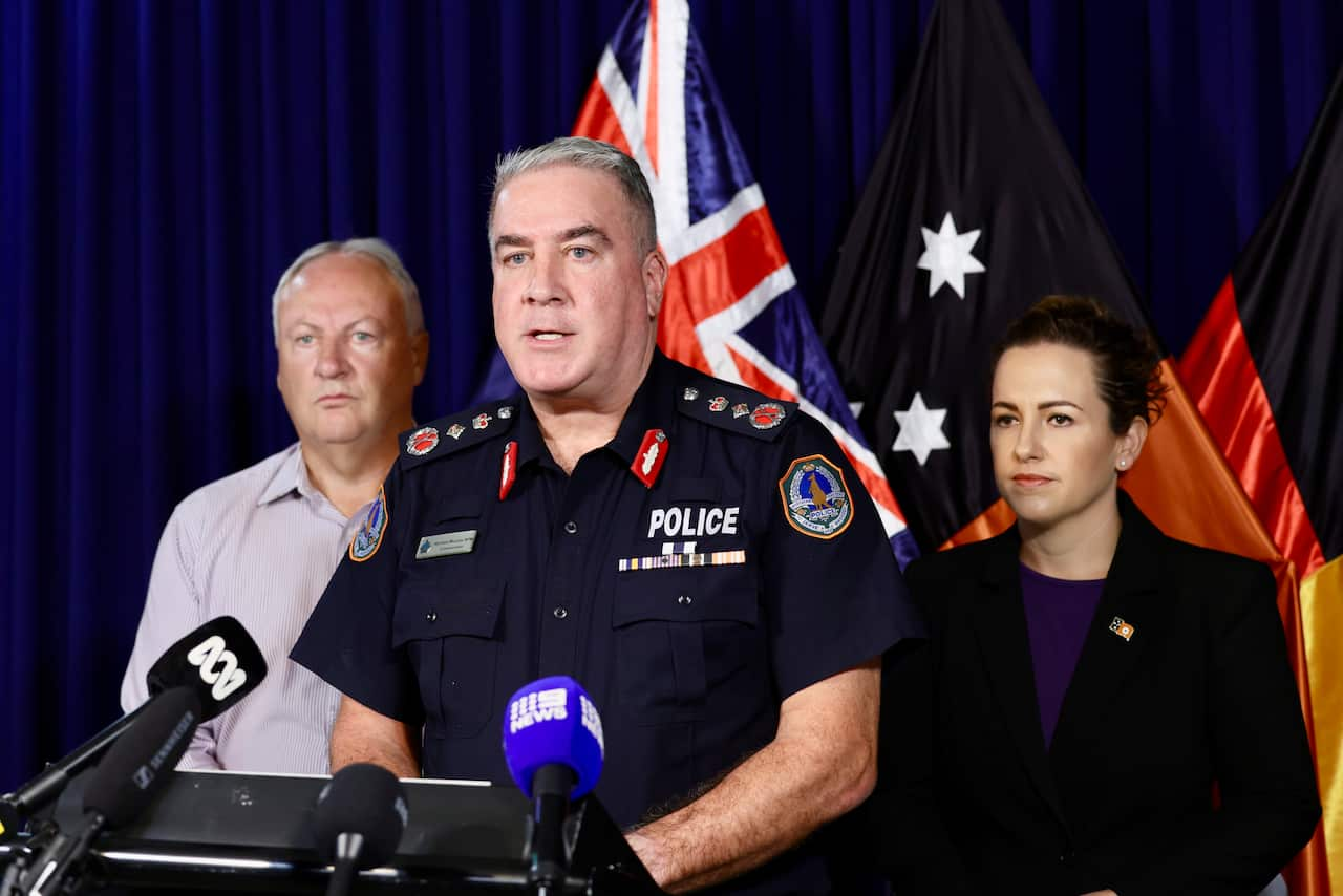 Two men and one woman stand in front of a podium and microphones.