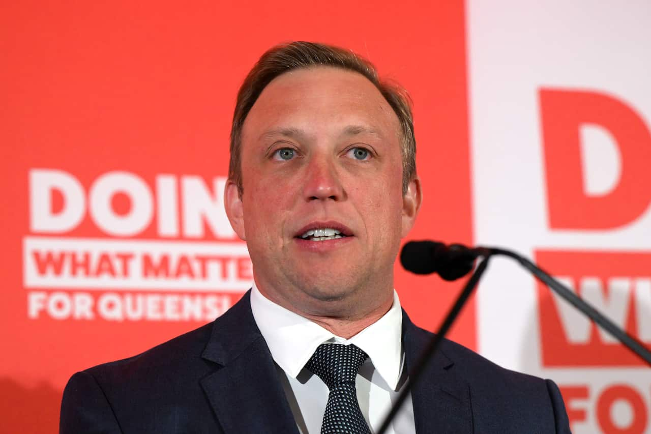 Steven Miles speaking into a microphone. Red signs behind him say "Doing What Matters for Queensland".