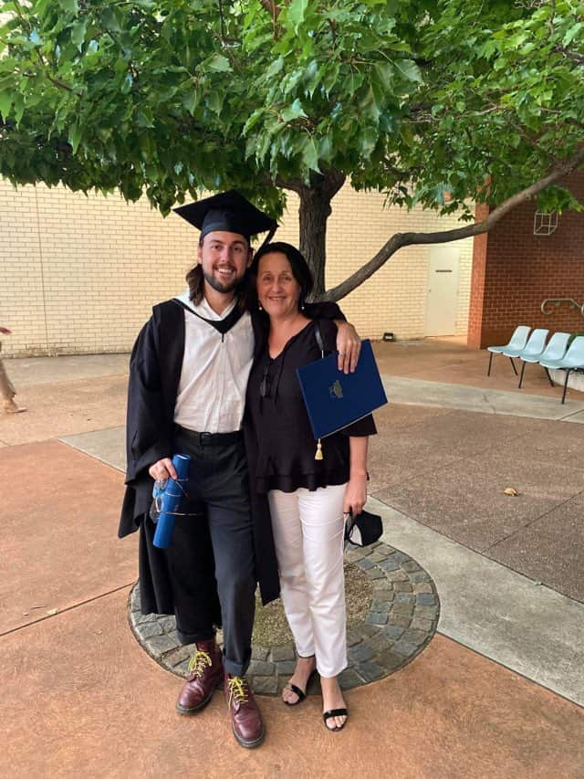 A man wearing a cap and gown standing with his mother 