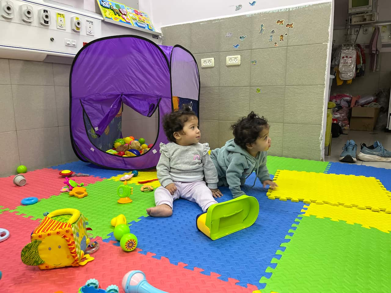 Two small children sit on a colourful playmat 