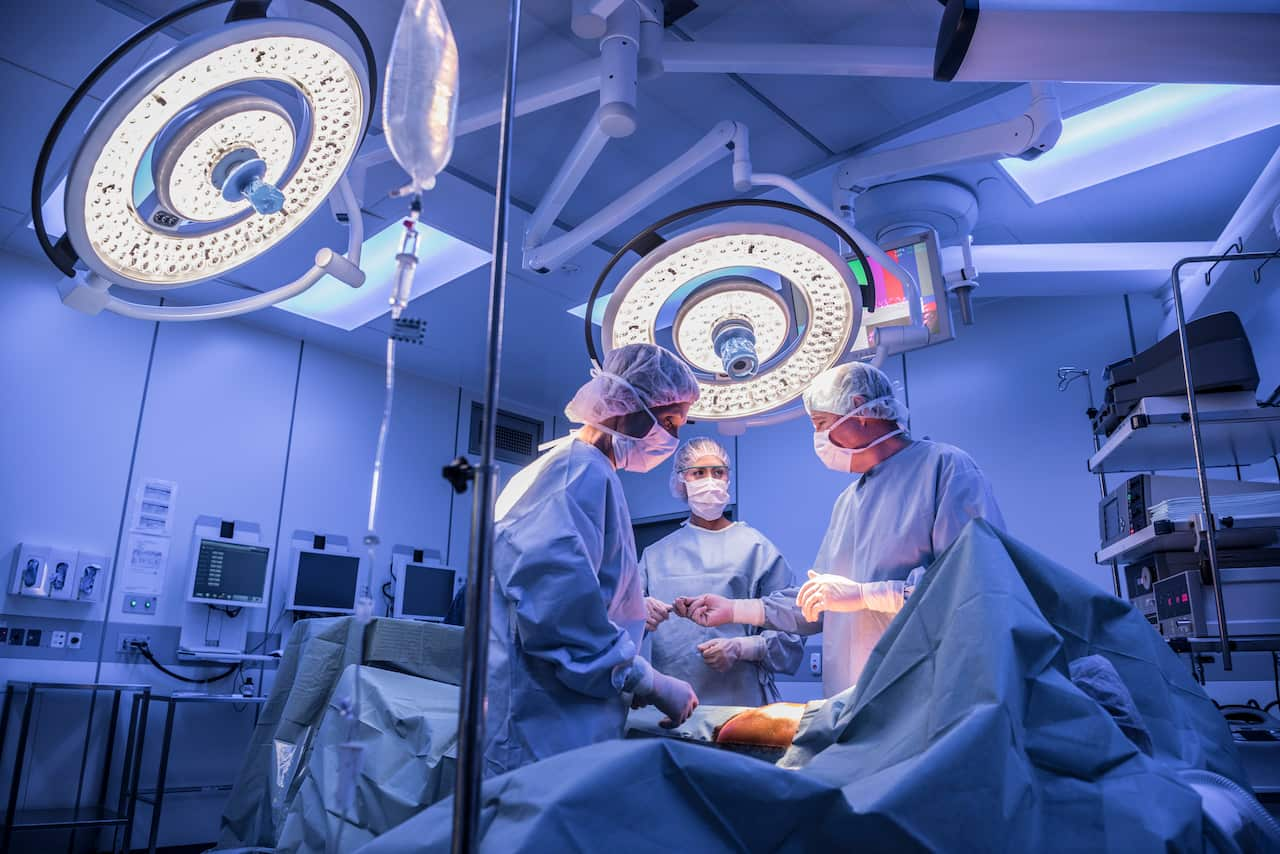 Surgeons operating on a patient in an operating theatre under lights.