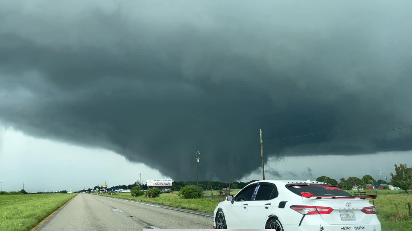 A car drives down a road, approaching a tornado.