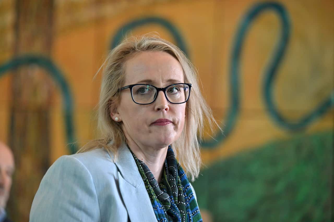 A woman standing inside wearing glasses and a blue blazer. 