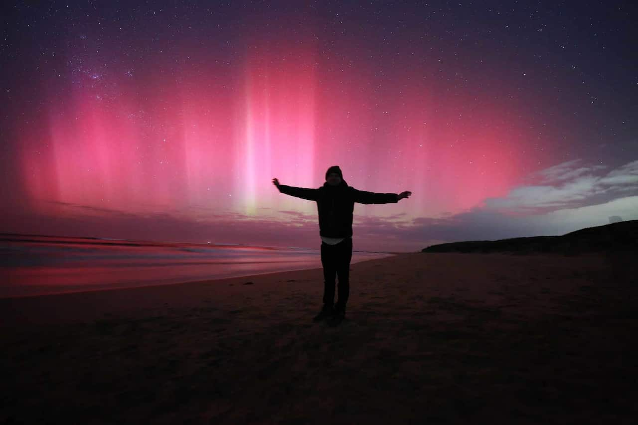 A silhouette of Arun, on a dark beach with the pink light of Aurora Australis behind him.