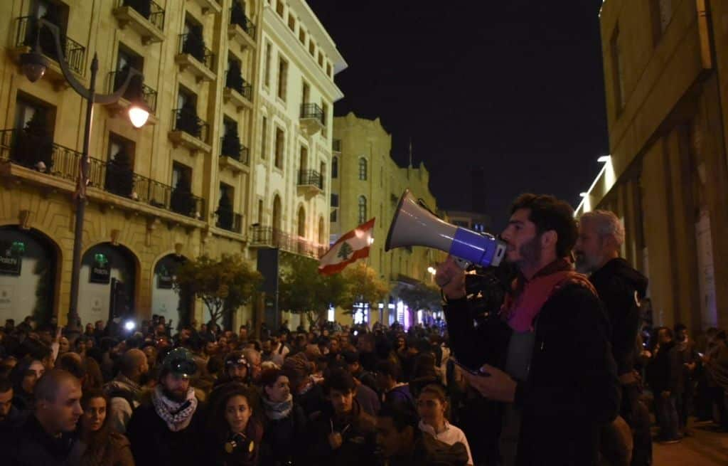 A man uses a megaphone to speak to protesters gathered in the street.