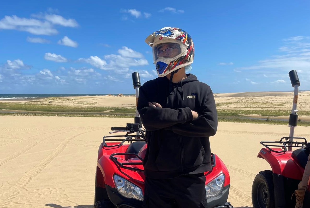 A man wearing black clothes and a motorcycle helmet leans against a quad bike.