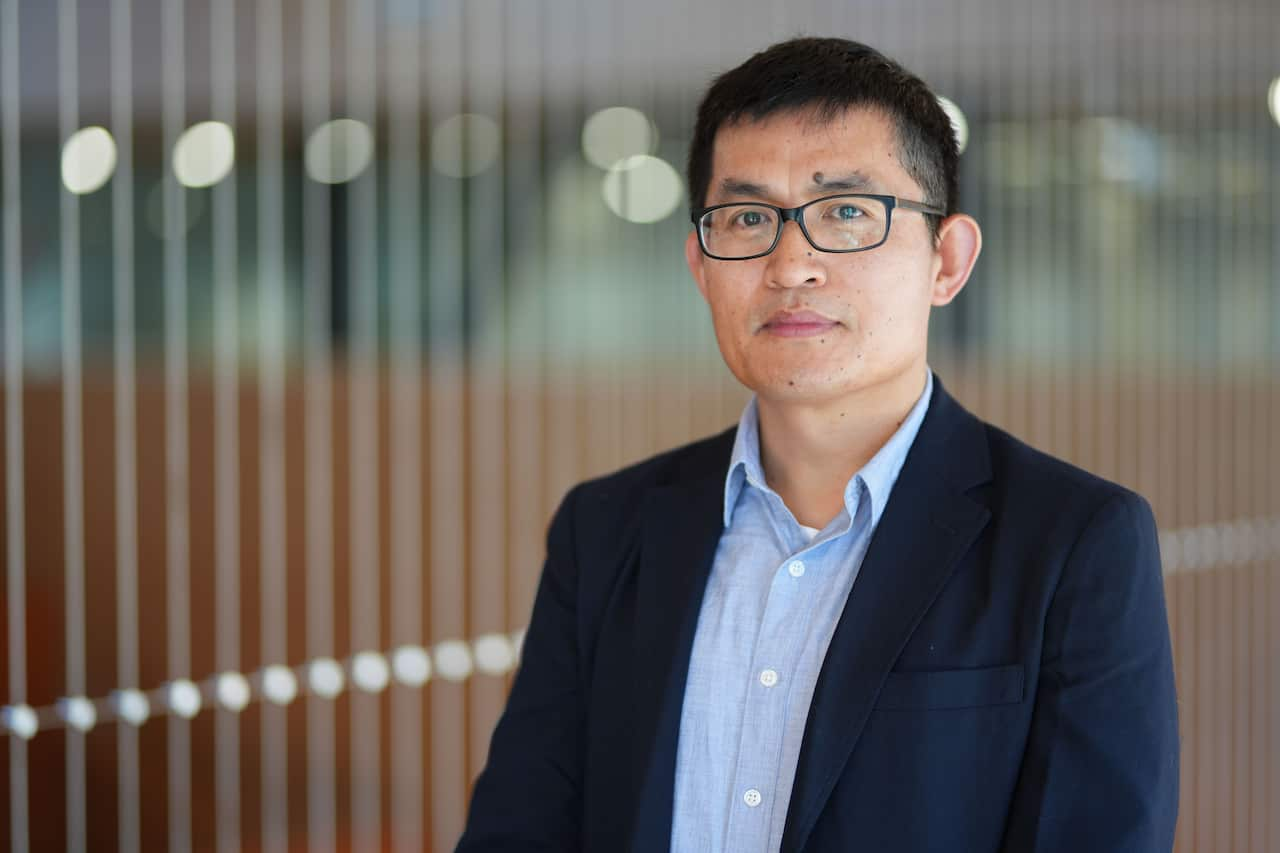 Dr Hongzhi Zhang, a middle-aged Chinese Australian man wearing a suit and glasses.