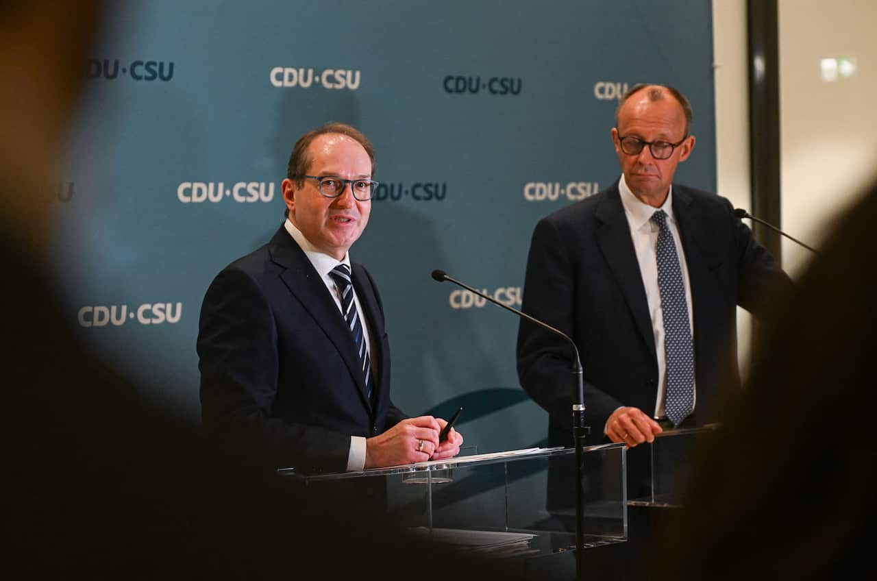 Two men in suits stand in front of microphones at a press conference.