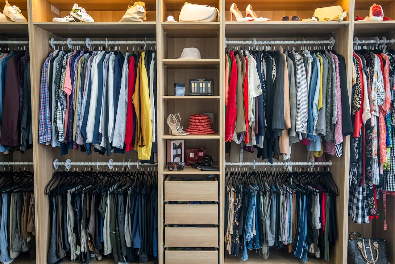 A walk-in wardrobe filled with clothes hanging, along with accessories and footwear arranged on shelves.