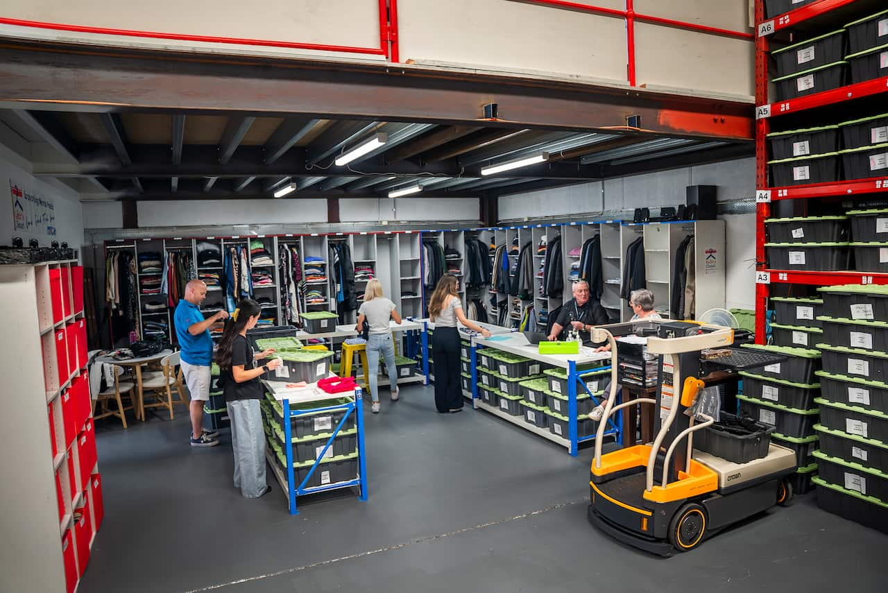 A small warehouse with clothing in shelves, people folding clothes and a forklift.