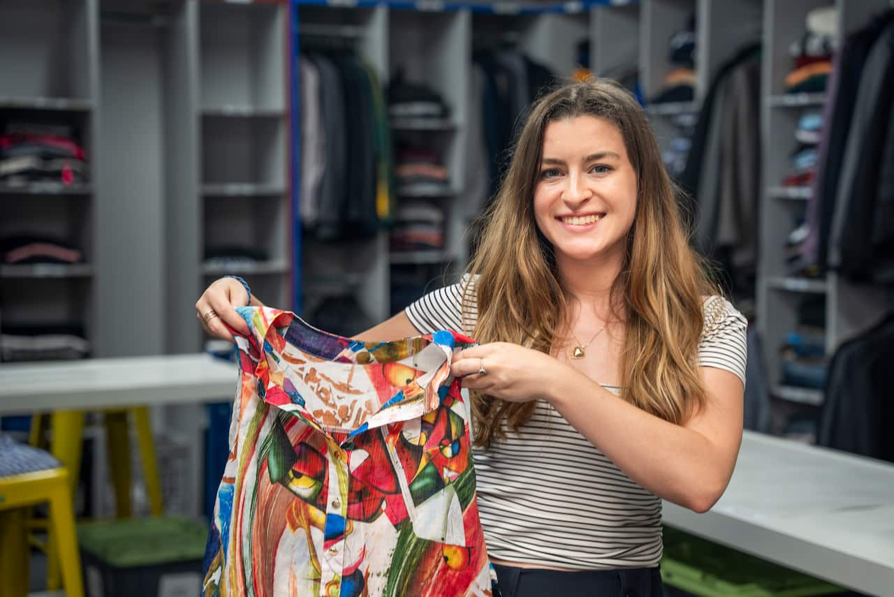 A woman holds a printed shirt and smiles at the camera.