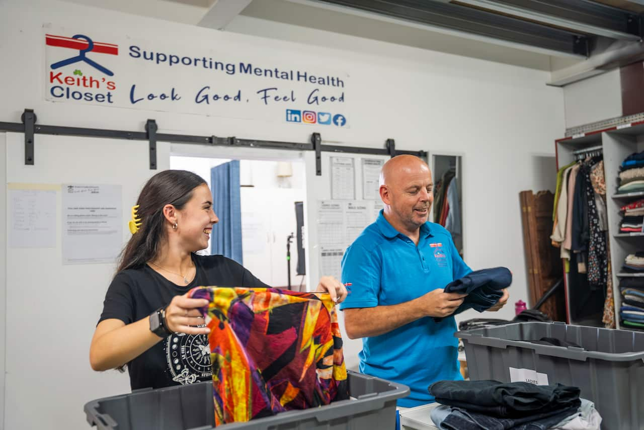 A man and a young woman folding clothes, smiling at each other and talking.