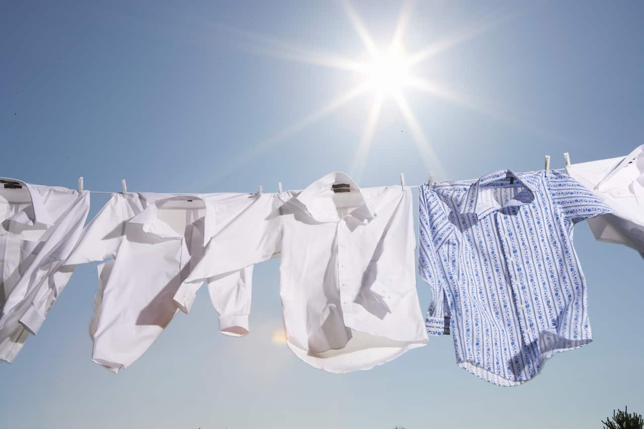 White shirts and one blue shirt hang from a washing line