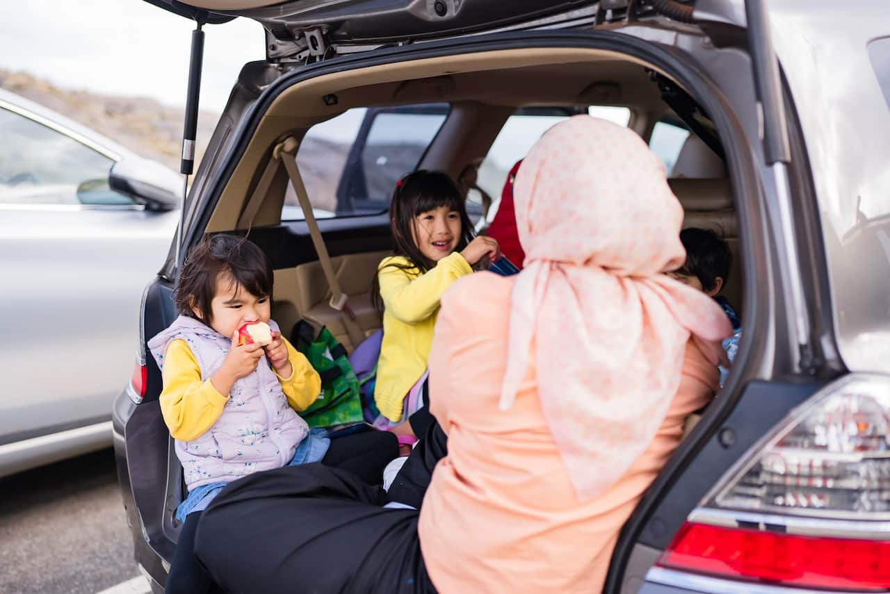 Two children sit in the open back of a wagon with a woman.