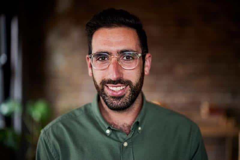 A man wearing glasses smiles at the camera.