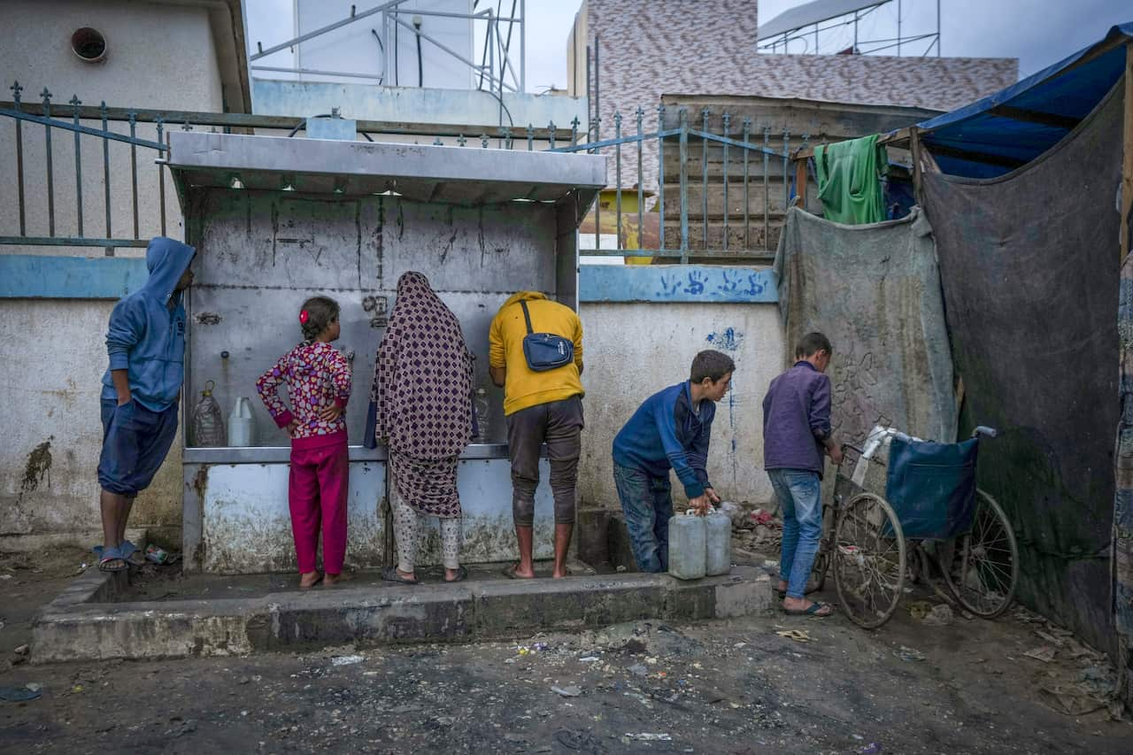 Six people in front of a steel kiosk-type structure from where they are filling containers with water