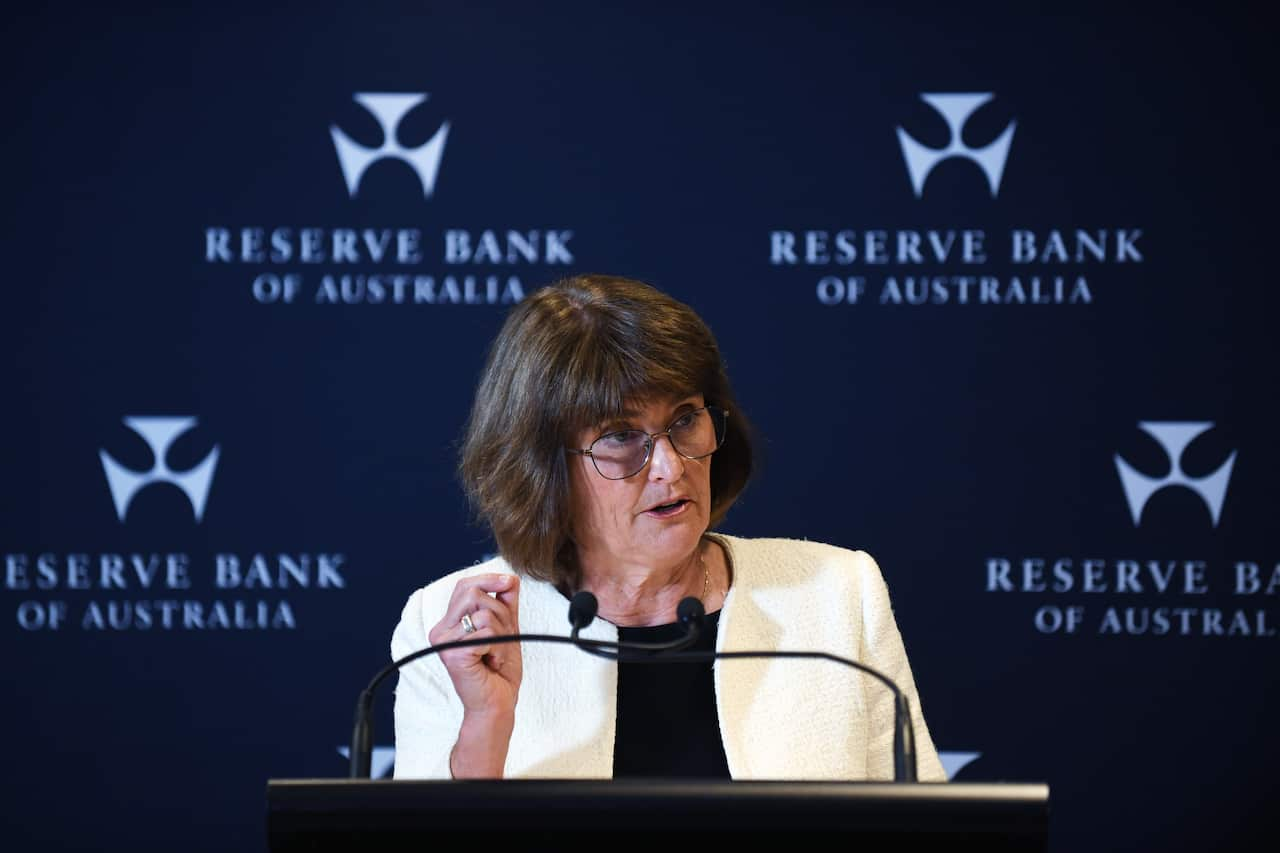 A woman in a white blazer stands at a podium with microphones in front of a sign that says 'Reserve Bank of Australia' 