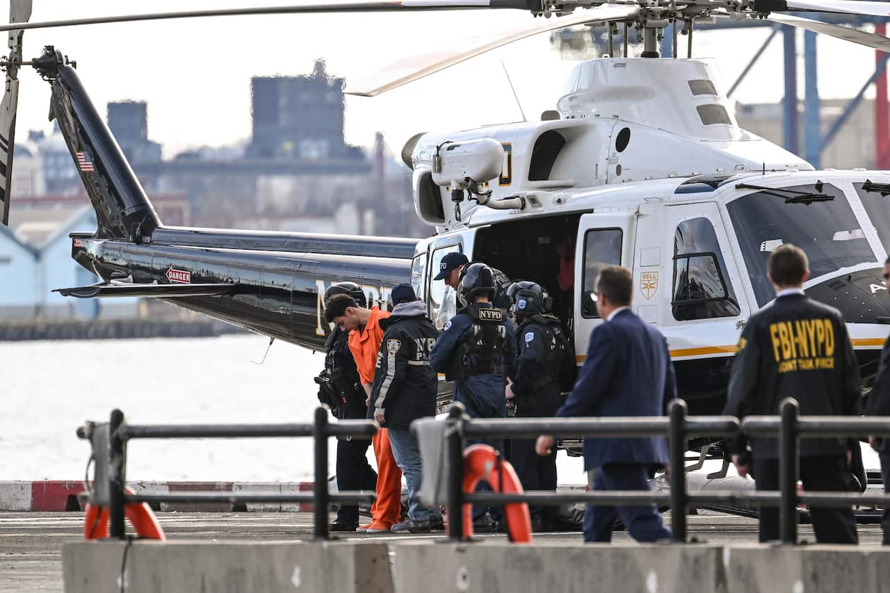 A man in an orange jumpsuit being taken off a helicopter by police.