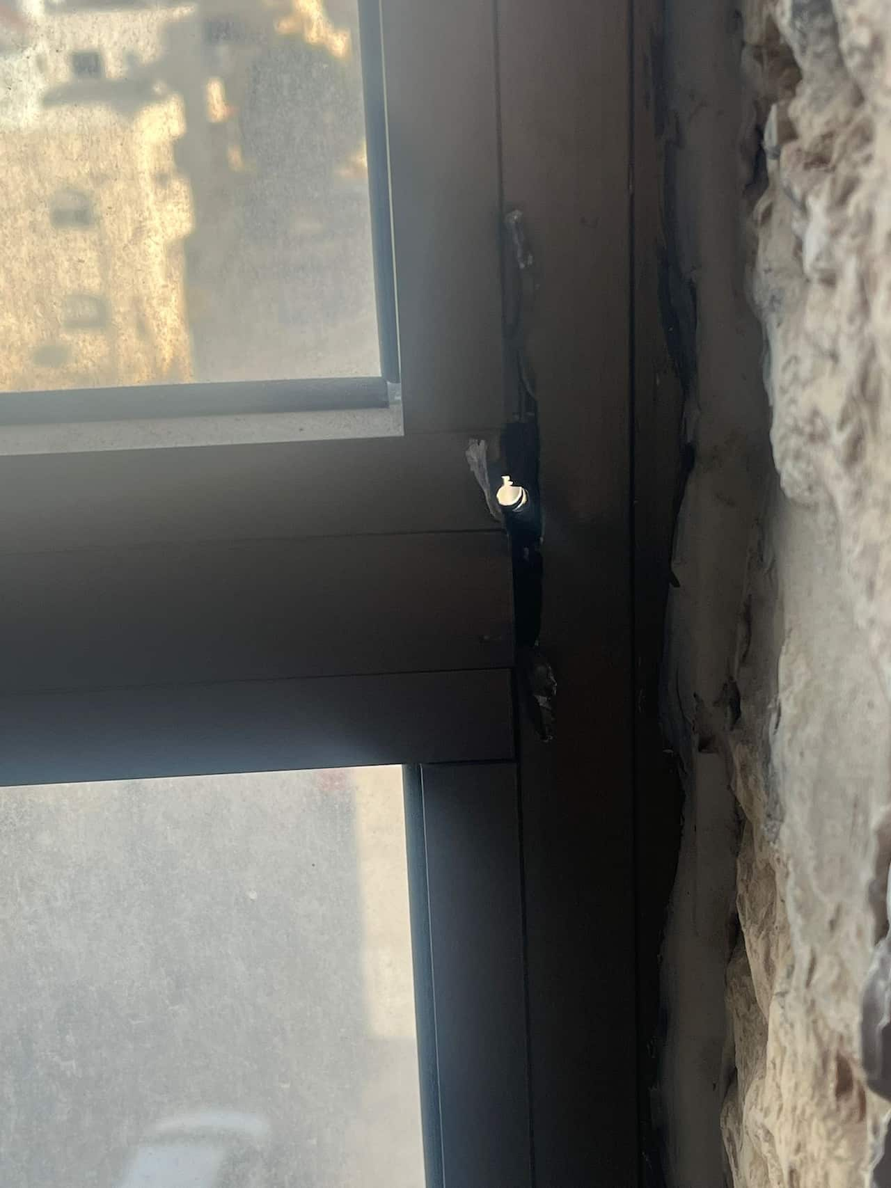 The corner of a window that is damaged and has a small hole in it.