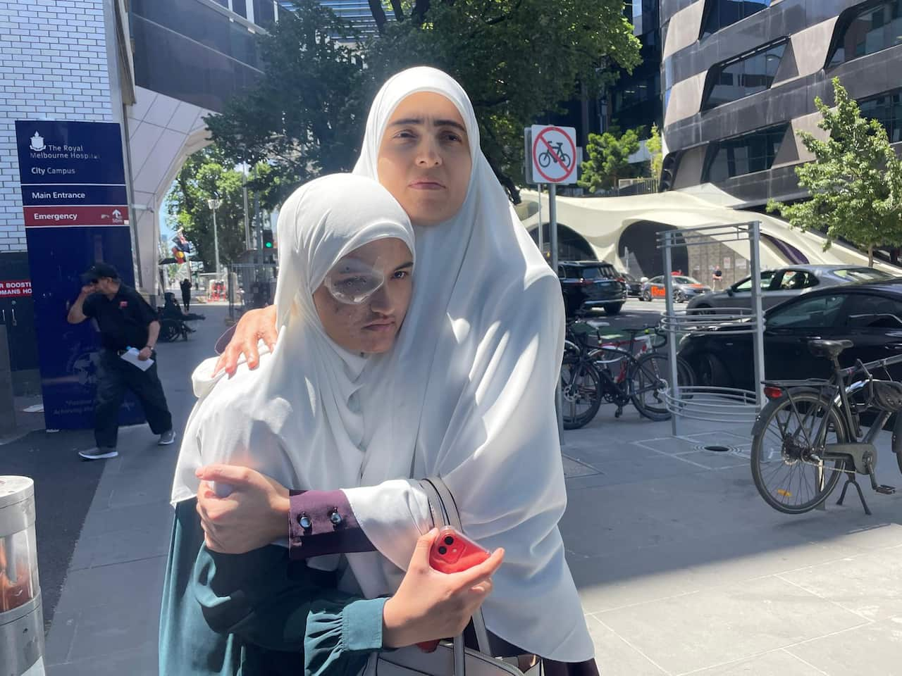 A woman hugs a younger woman. Both wear flowing white headdresses. 