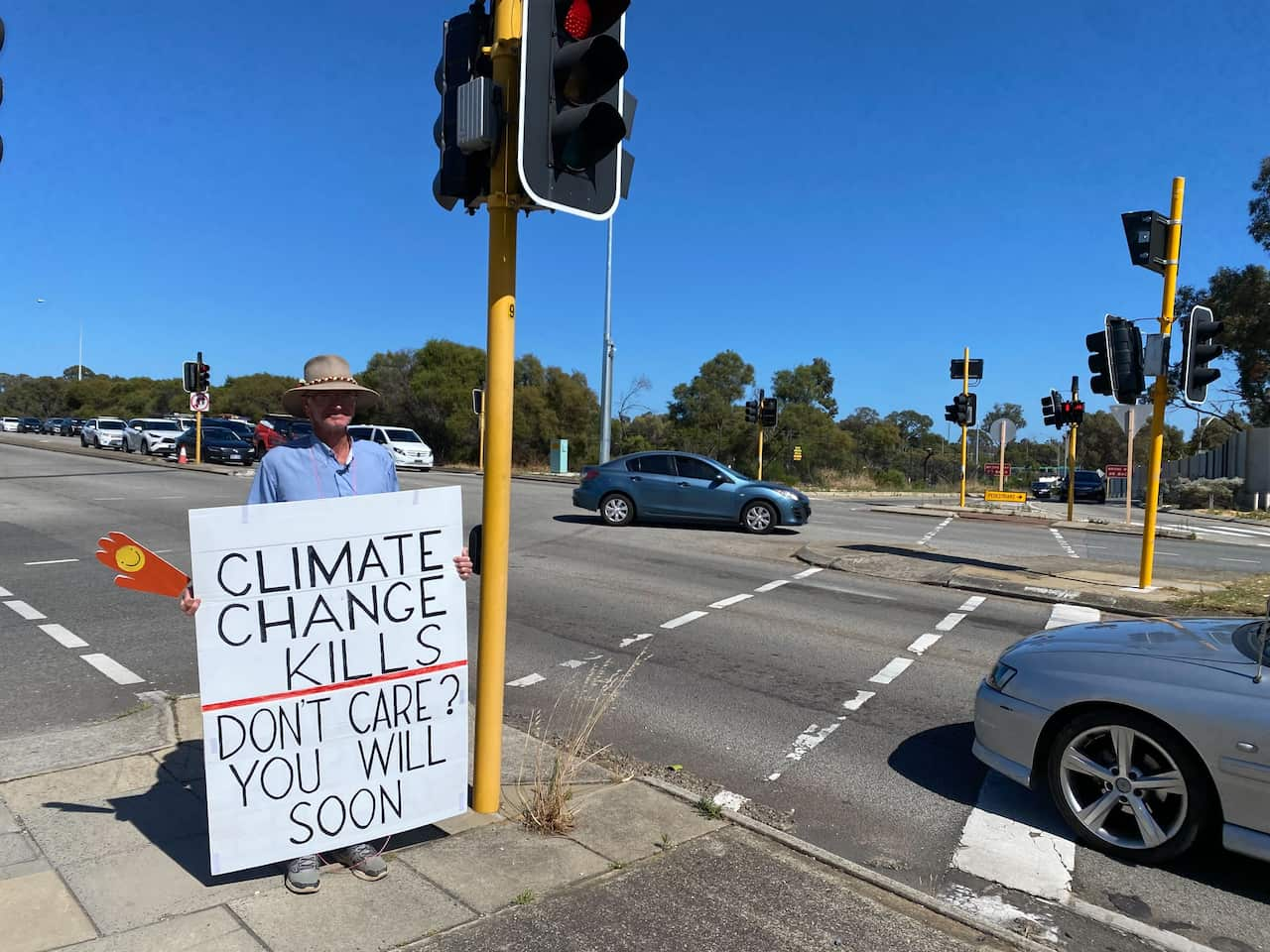 A man beside a busy intersection, holding a sign that reads 'Climate change kills, don't care? You will soon.'