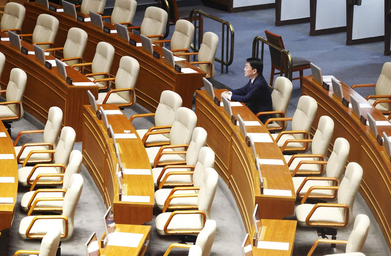 A Korean man sitting along in a parliamentary chamber