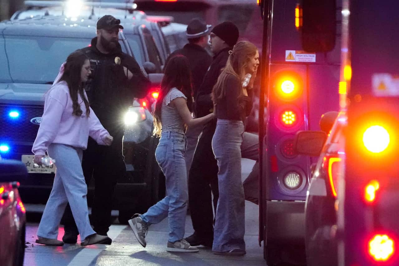 Teens are boarding a police bus with its tail lights on, while police officials stand next to one of the buses.