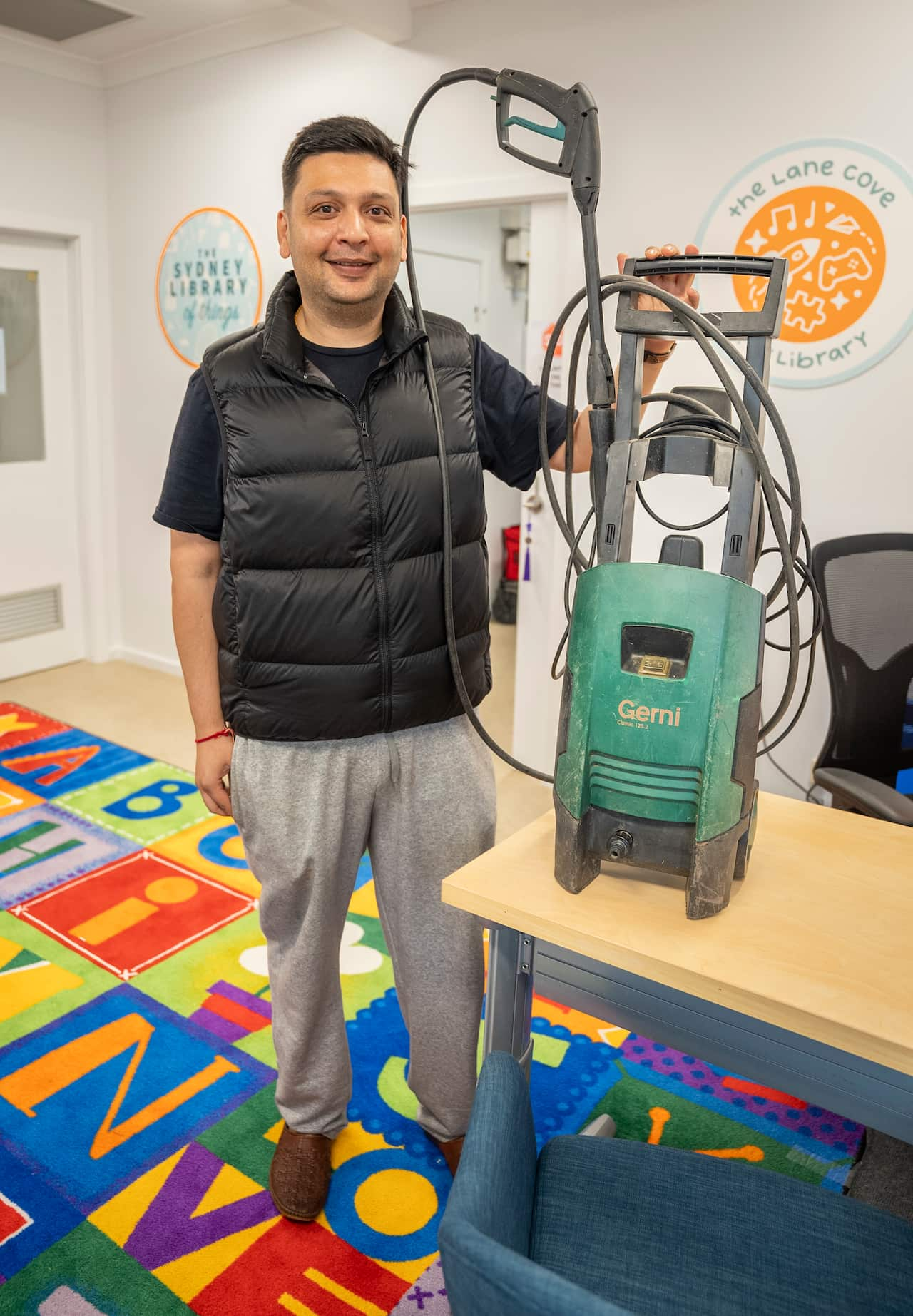 A man smiling standing next to a green high pressure washer on a work bench