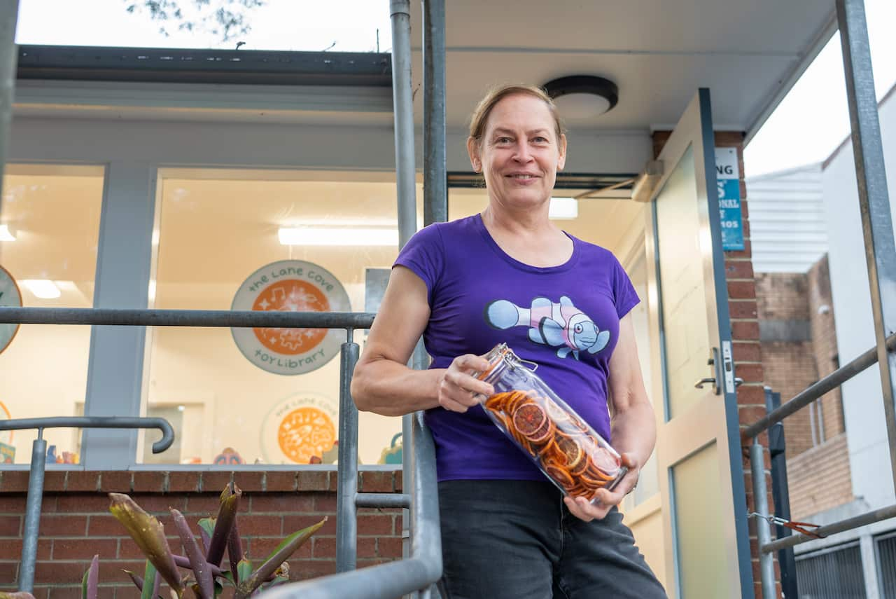 A woman in front of a building holding a jar of dried oranges