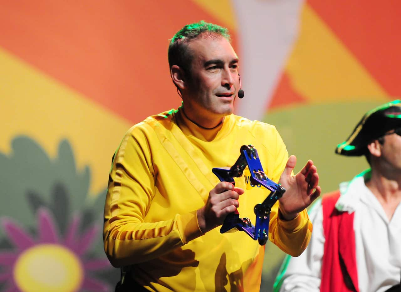 A man wearing a yellow crewneck t-shirt performs on stage, holding a star-shaped tambourine. 