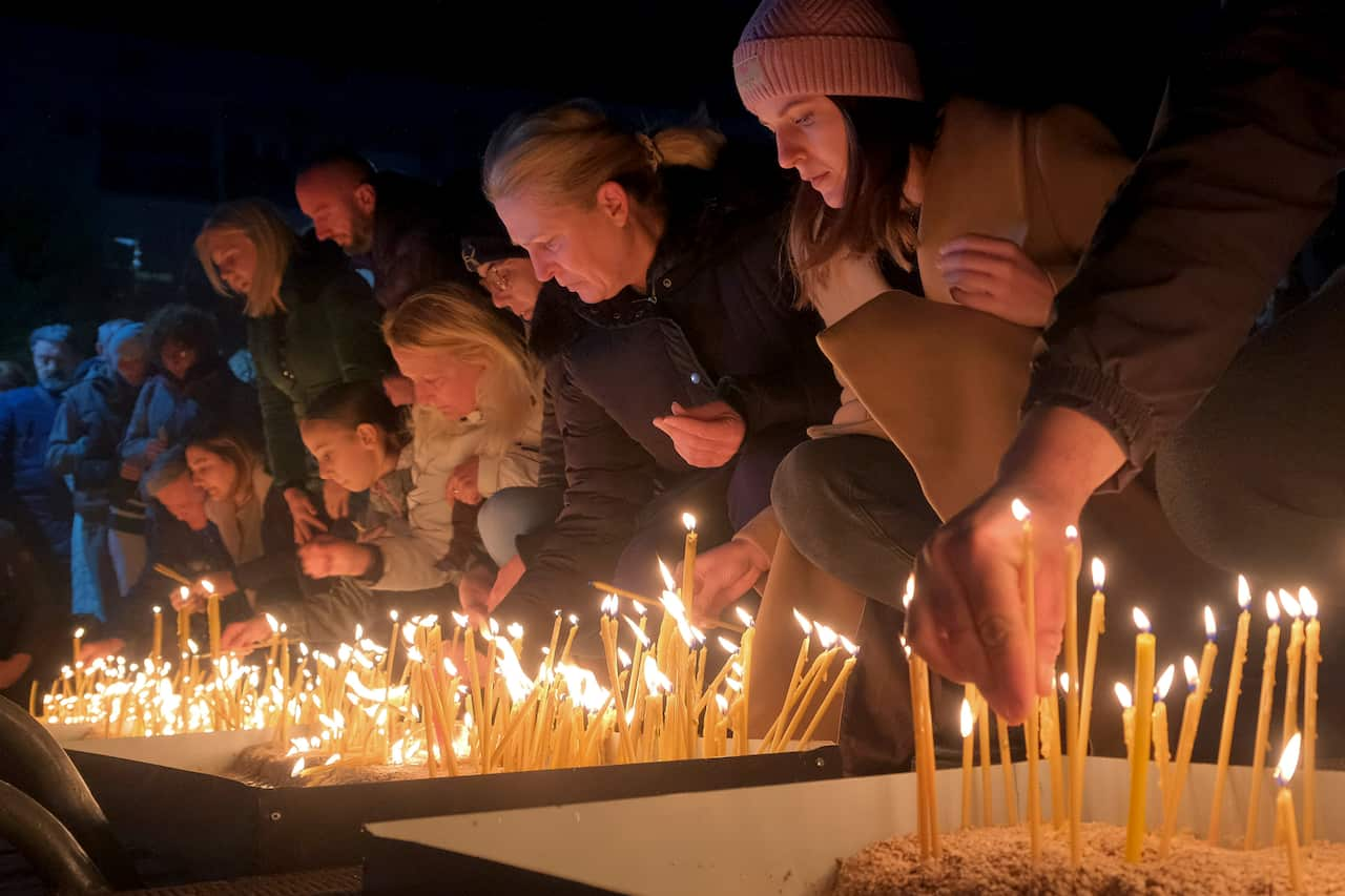 People kneeling down and lighting candles.