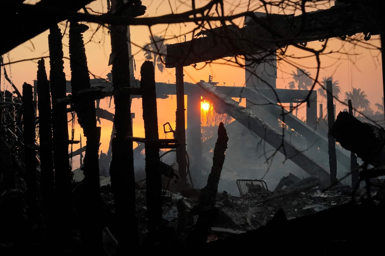 The frame of a burned out building in front of a rising sun.