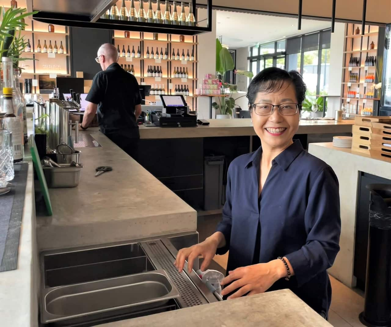 A woman in a blue shirt stands at the sink in a winery.